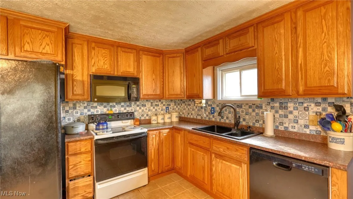 Kitchen with decorative backsplash, brown cabinetry, light tile patterned flooring, a sink, and black appliances