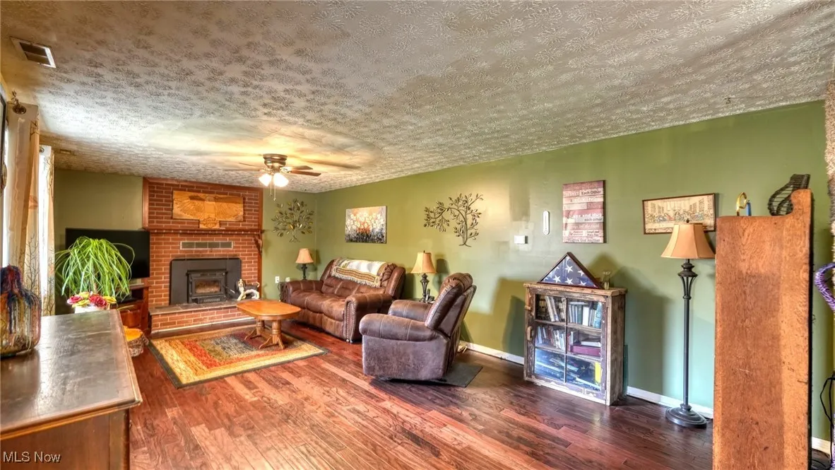 Living area with visible vents, a ceiling fan, a textured ceiling, wood finished floors, and baseboards