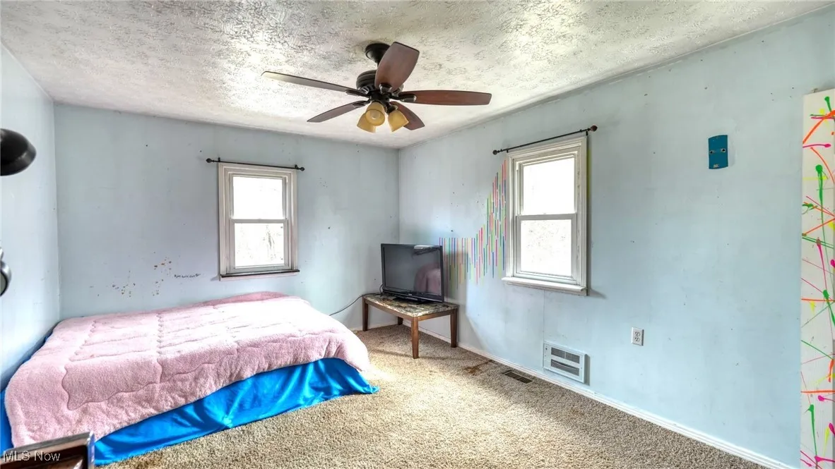 Carpeted bedroom featuring a textured ceiling, multiple windows, and visible vents