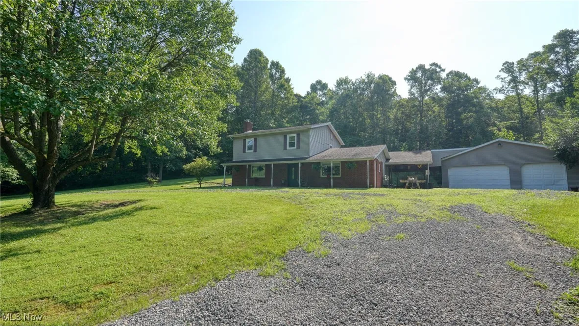 View of front of property featuring a garage, a chimney, a front lawn, gravel driveway, and covered porch