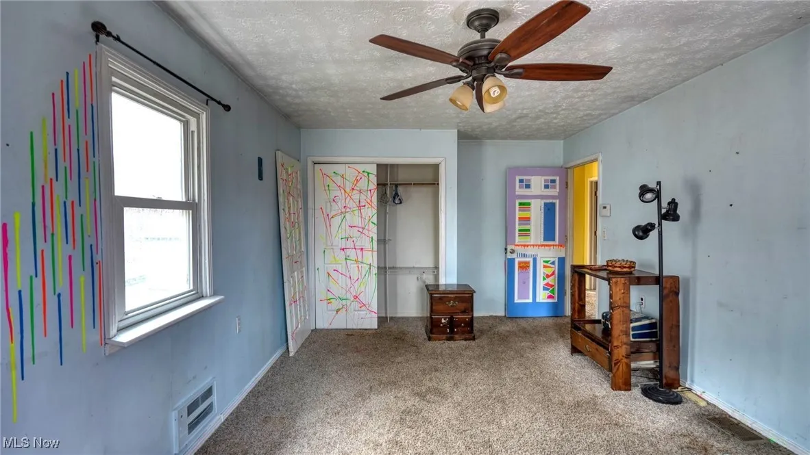Carpeted bedroom featuring a textured ceiling, ceiling fan, a closet, and visible vents