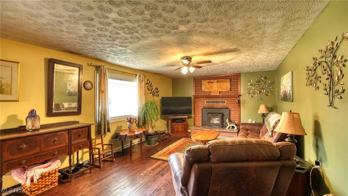 Living area featuring a wood stove, wood-type flooring, ceiling fan, and a textured ceiling