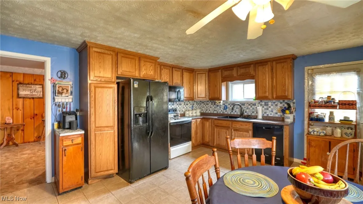Kitchen with tasteful backsplash, brown cabinetry, a textured ceiling, black appliances, and a sink