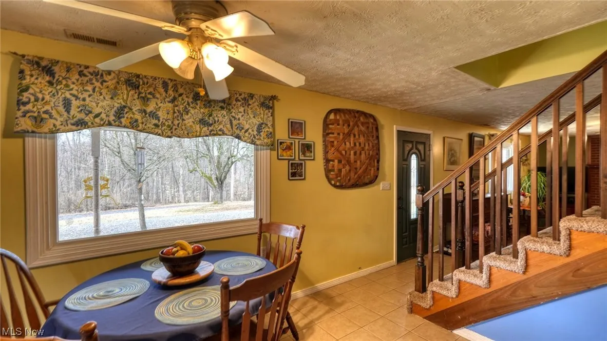 Dining area featuring light tile patterned floors, a textured ceiling, visible vents, baseboards, and stairs