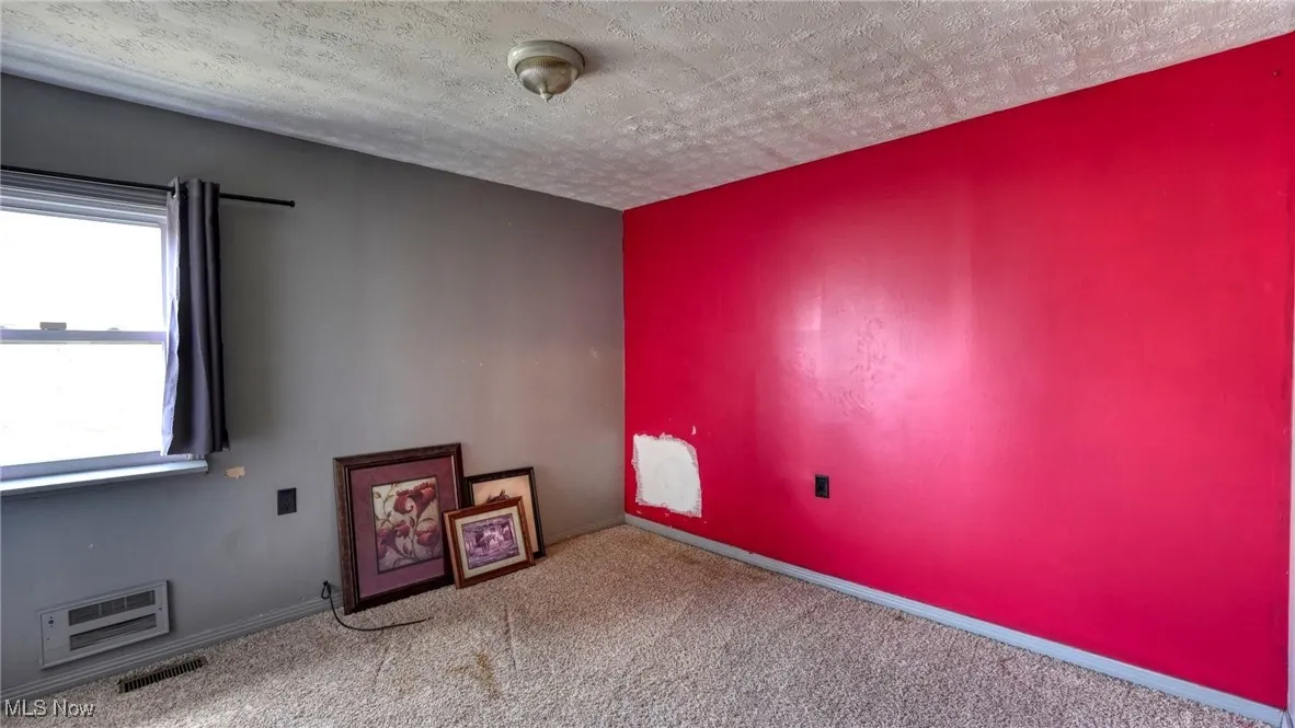 Carpeted empty room featuring visible vents, a textured ceiling, and baseboards