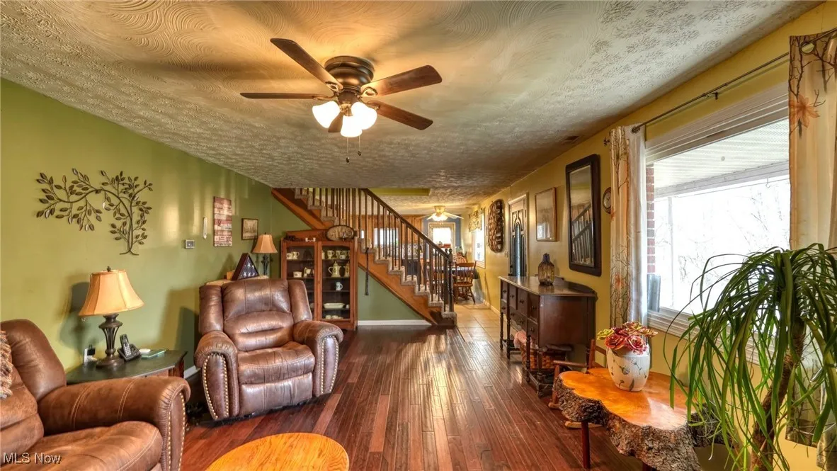 Living area featuring a textured ceiling, ceiling fan, stairway, and wood-type flooring