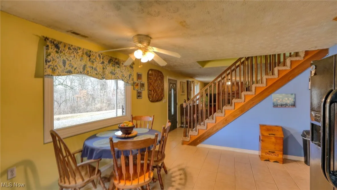 Dining room with a textured ceiling, a ceiling fan, visible vents, stairs, and baseboards