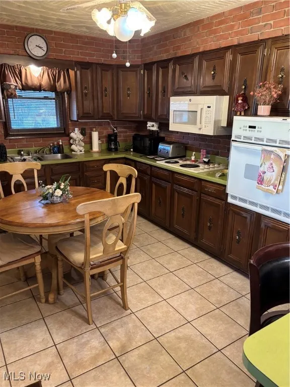 Kitchen with dark brown cabinetry, tasteful backsplash, brick wall, oven, and light countertops