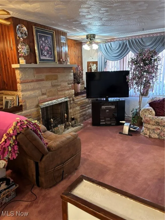 Living room featuring carpet floors, a ceiling fan, and a stone fireplace