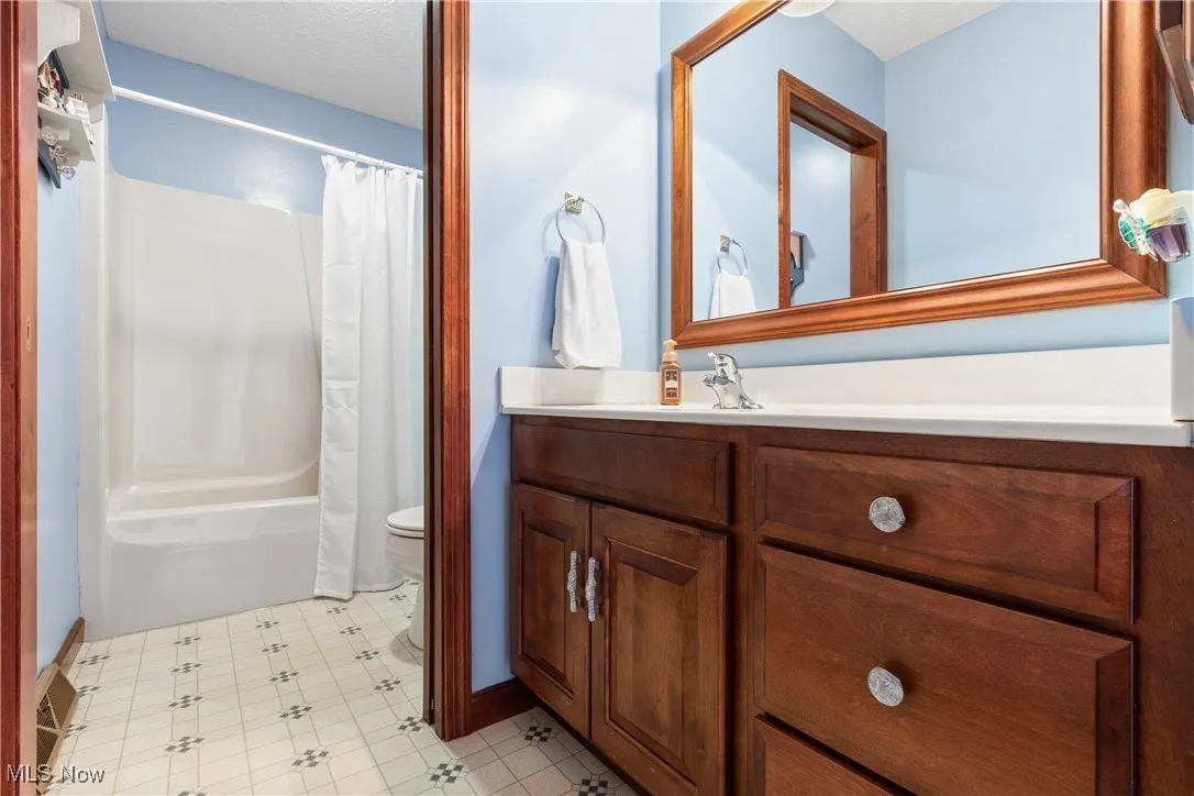 Full bath with a textured ceiling, toilet, vanity, tile patterned floors, and shower / bathtub combination with curtain