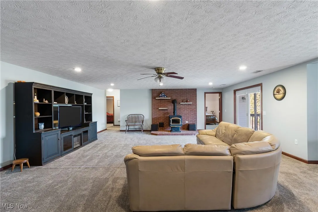 Living room with a textured ceiling, recessed lighting, light colored carpet, baseboards, and a wood stove