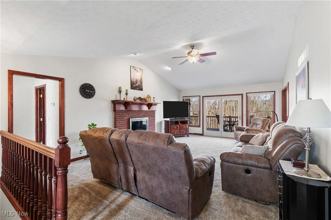Carpeted living room featuring baseboards, a ceiling fan, vaulted ceiling, a textured ceiling, and a fireplace