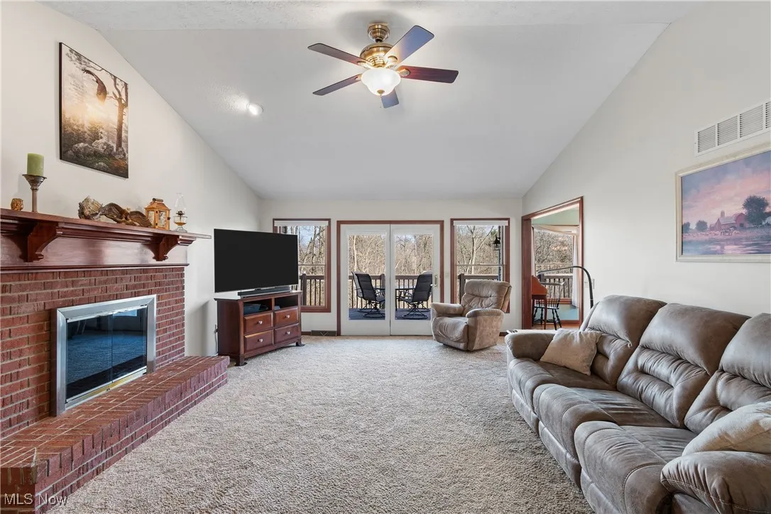 Carpeted living room with high vaulted ceiling, a brick fireplace, visible vents, and ceiling fan