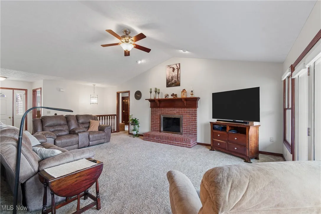 Carpeted living area with lofted ceiling, ceiling fan, a fireplace, and baseboards