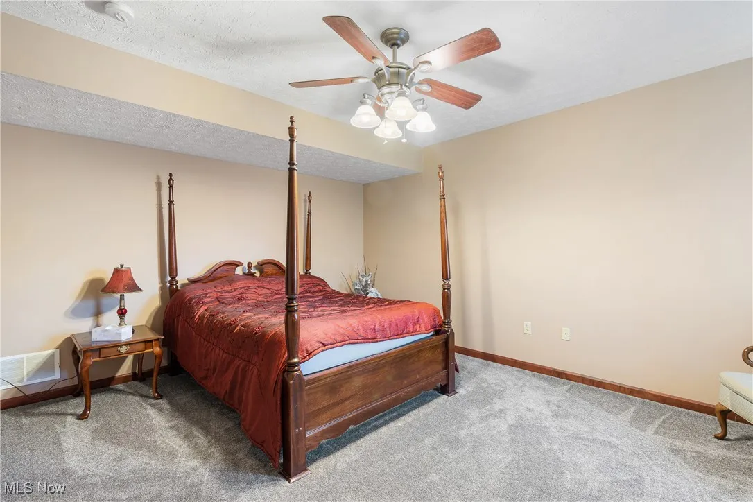 Bedroom with a textured ceiling, carpet flooring, visible vents, a ceiling fan, and baseboards