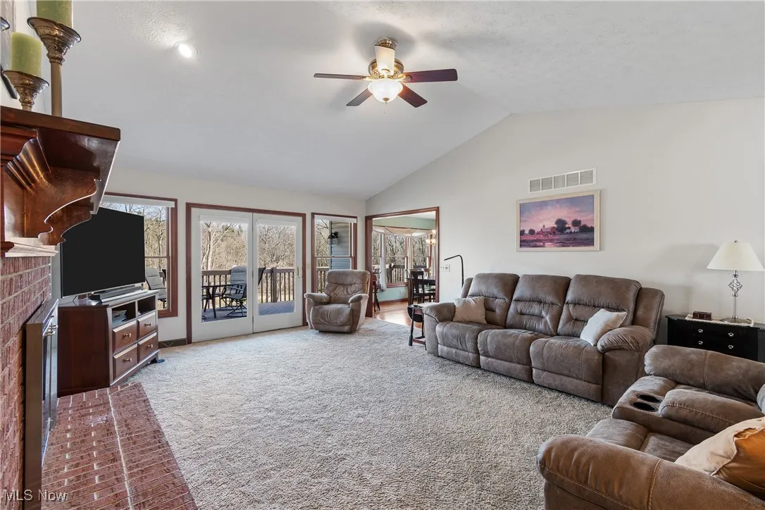 Carpeted living room with high vaulted ceiling, a fireplace, visible vents, and a ceiling fan