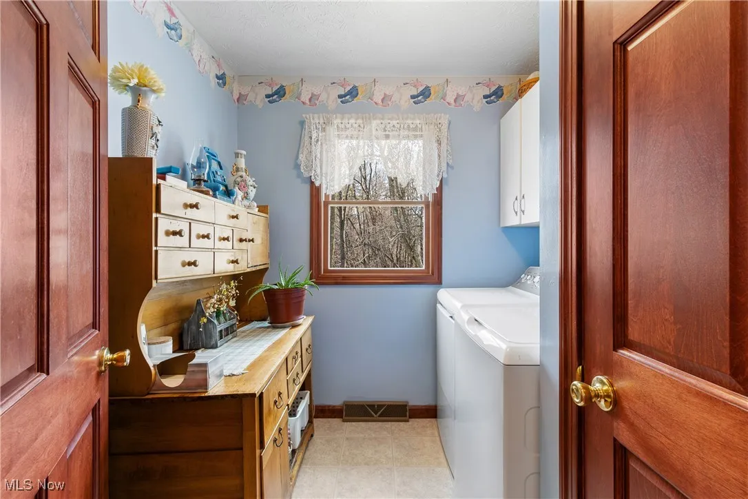 Washroom featuring cabinet space, visible vents, baseboards, washer and clothes dryer, and light tile patterned flooring