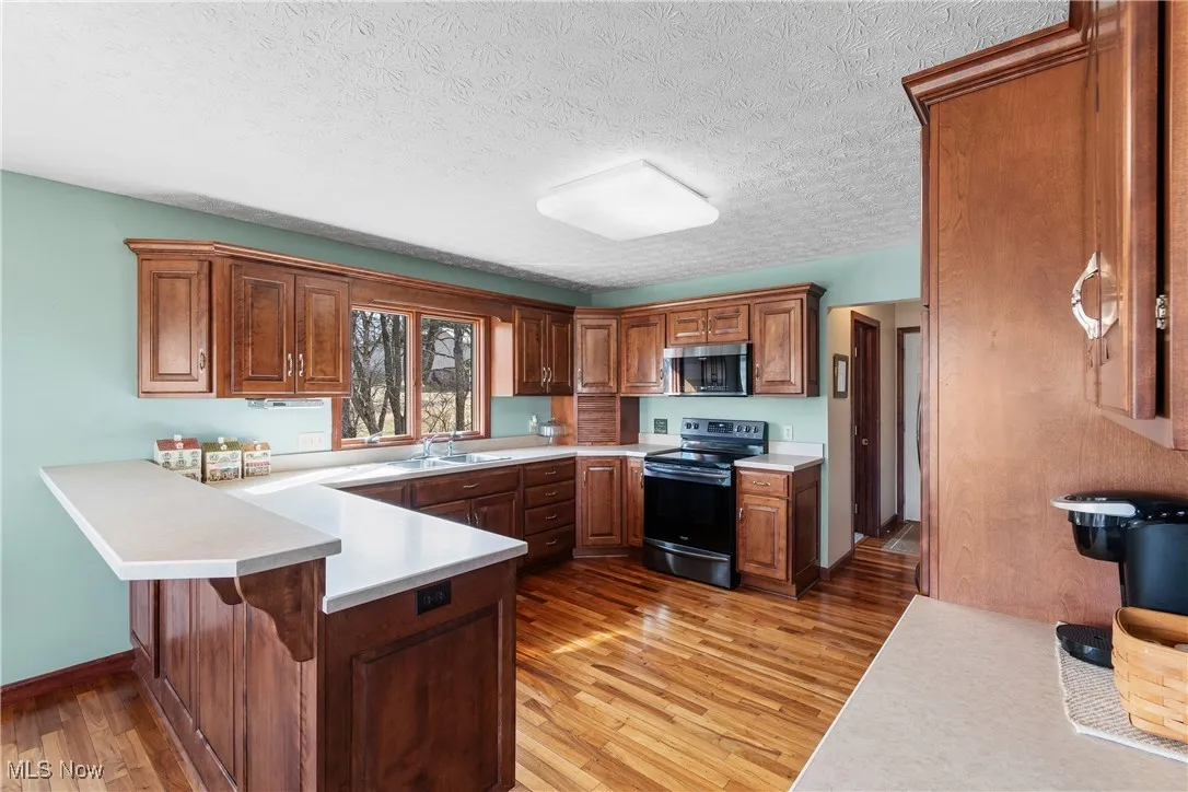 Kitchen with light wood finished floors, stainless steel appliances, light countertops, a sink, and a peninsula