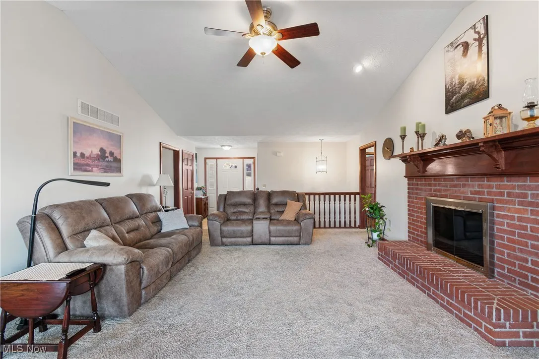 Carpeted living area featuring ceiling fan, high vaulted ceiling, a fireplace, and visible vents