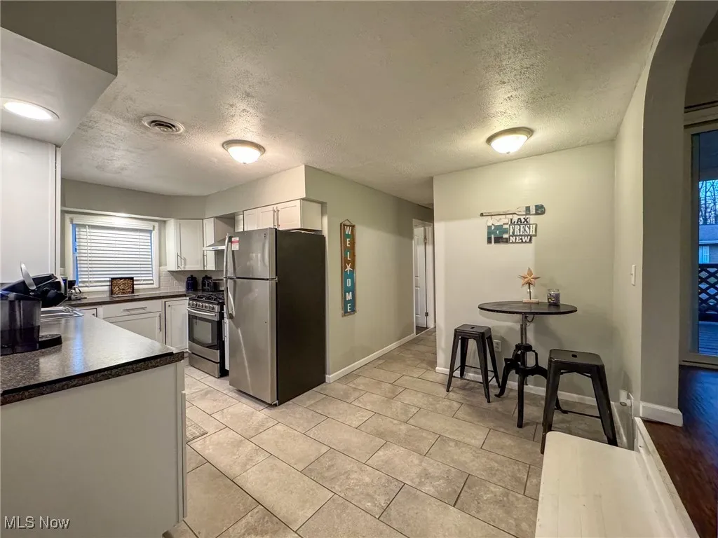 Kitchen with visible vents, dark countertops, appliances with stainless steel finishes, wall chimney range hood, and white cabinetry