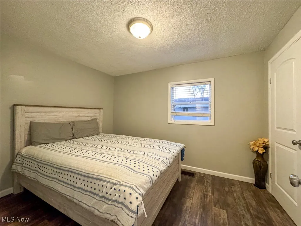 Bedroom with a textured ceiling, wood finished floors, visible vents, and baseboards