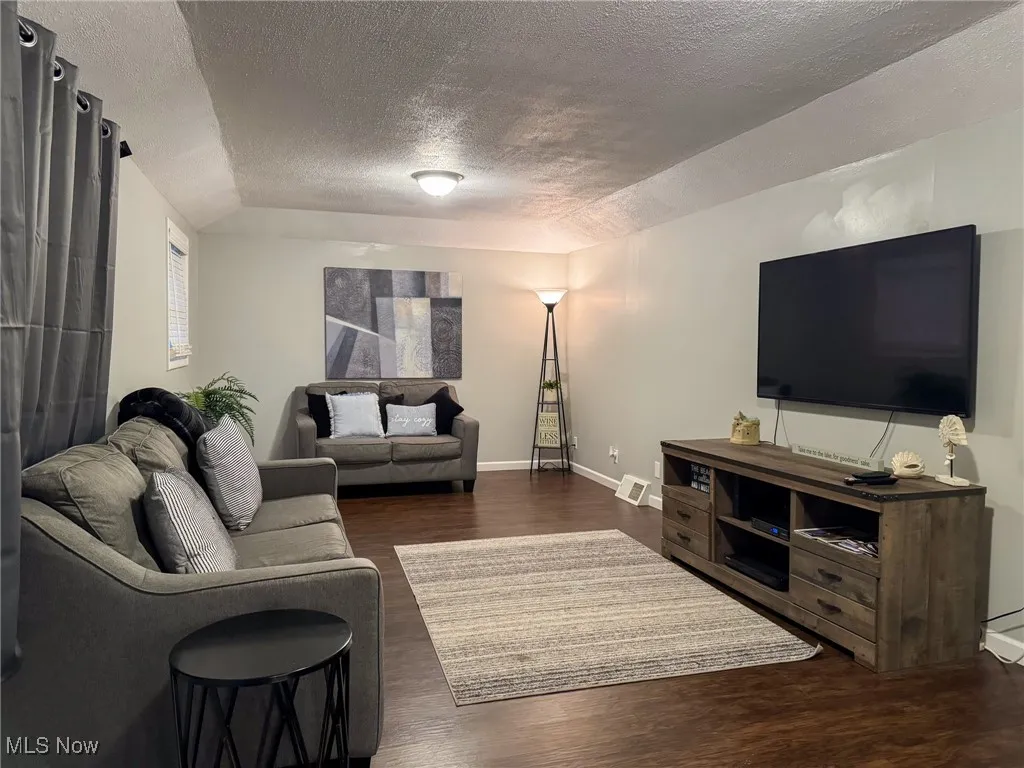 Living area featuring baseboards, a textured ceiling, visible vents, and wood finished floors