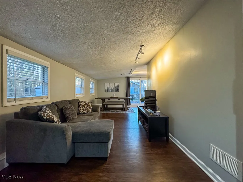 Living room featuring dark wood finished floors, rail lighting, visible vents, a textured ceiling, and baseboards