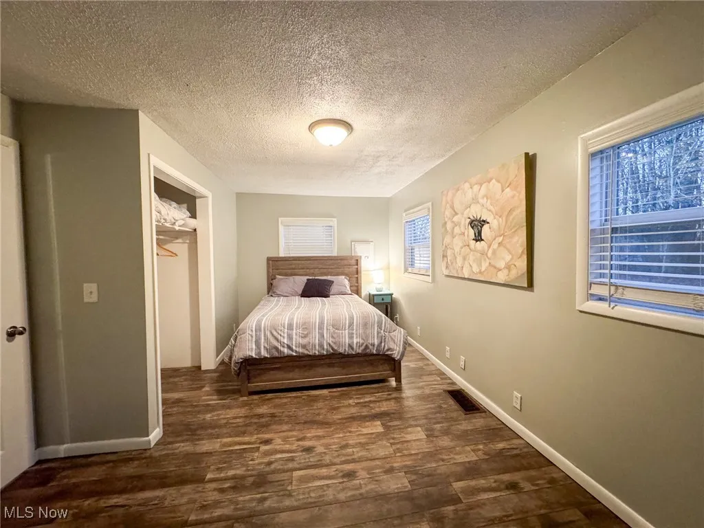 Bedroom featuring a textured ceiling, wood finished floors, visible vents, and baseboards