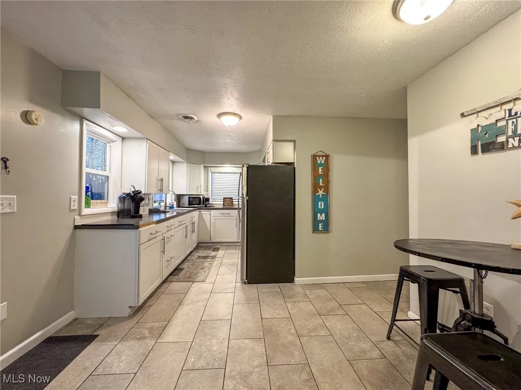 Kitchen featuring a textured ceiling, stainless steel appliances, baseboards, white cabinets, and dark countertops
