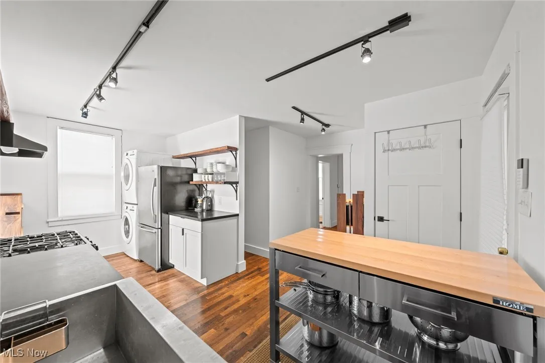 Kitchen with stacked washer and clothes dryer, open shelves, rail lighting, freestanding refrigerator, and wood finished floors