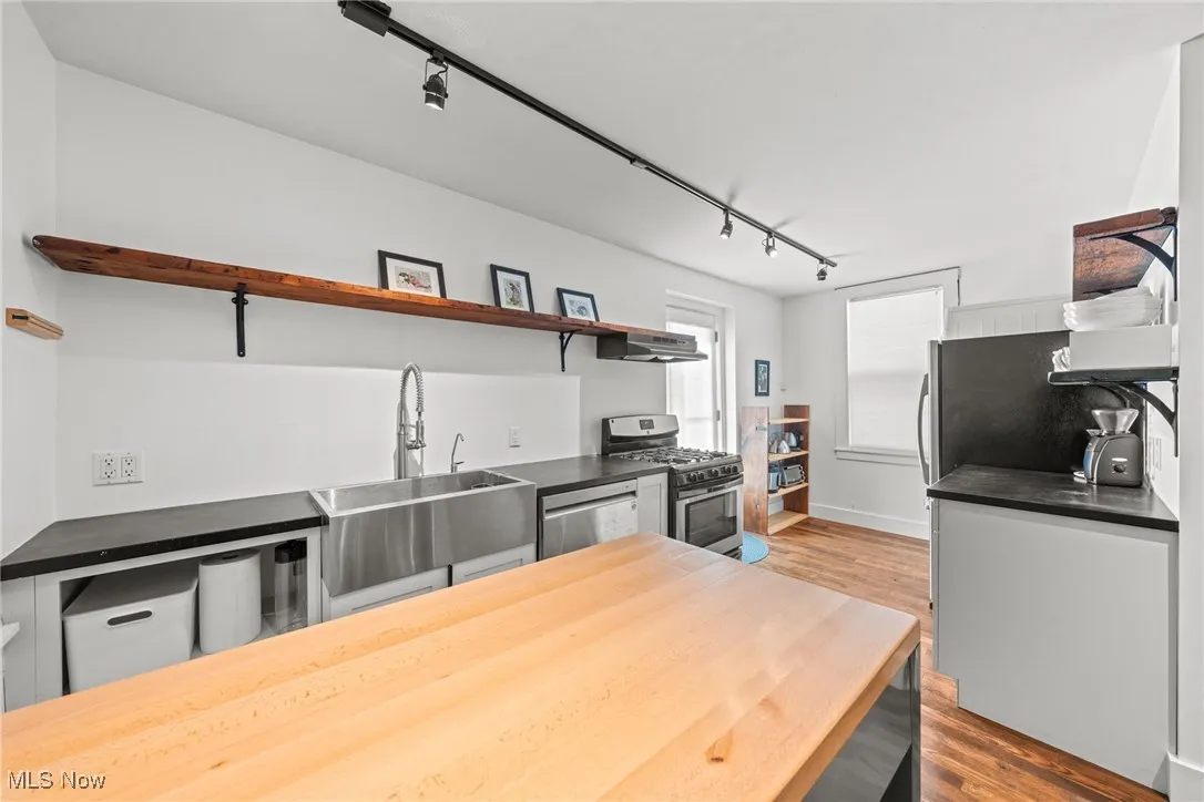 Kitchen featuring under cabinet range hood, stainless steel appliances, a sink, wood finished floors, and open shelves