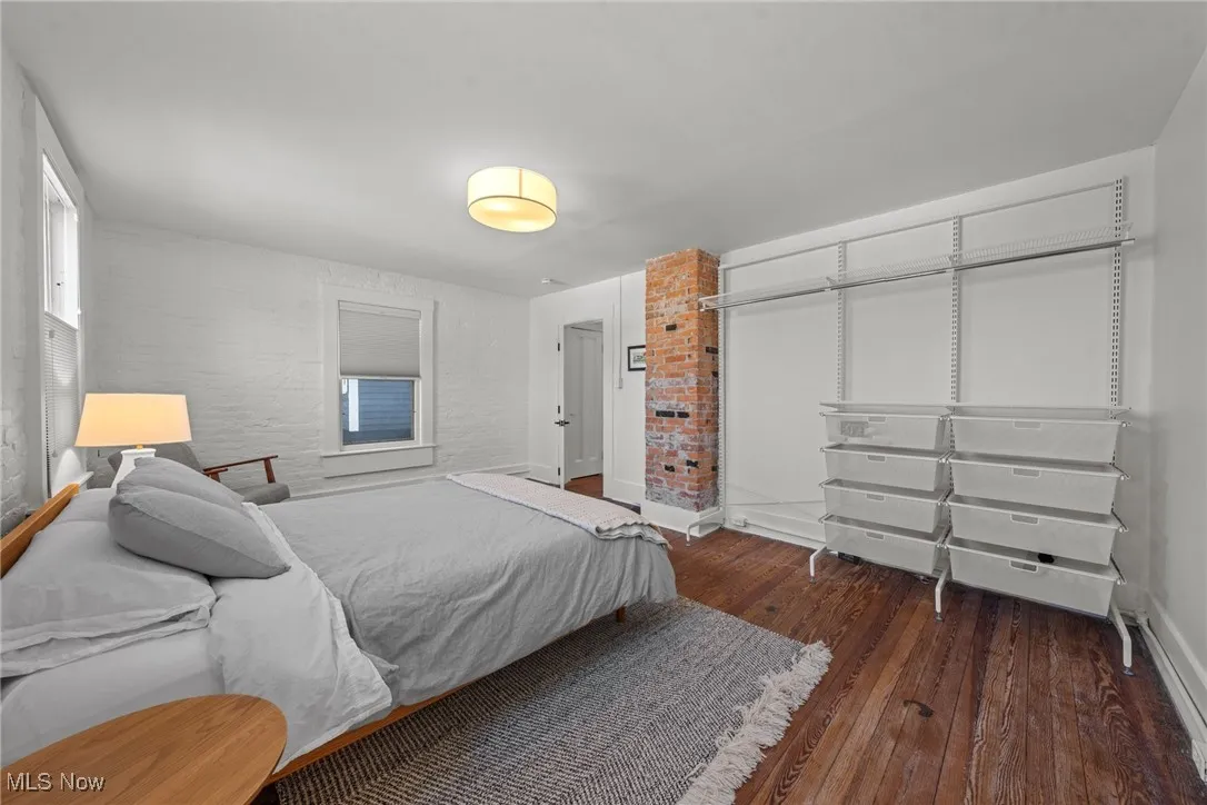 Bedroom featuring wood-type flooring, brick wall, and baseboards