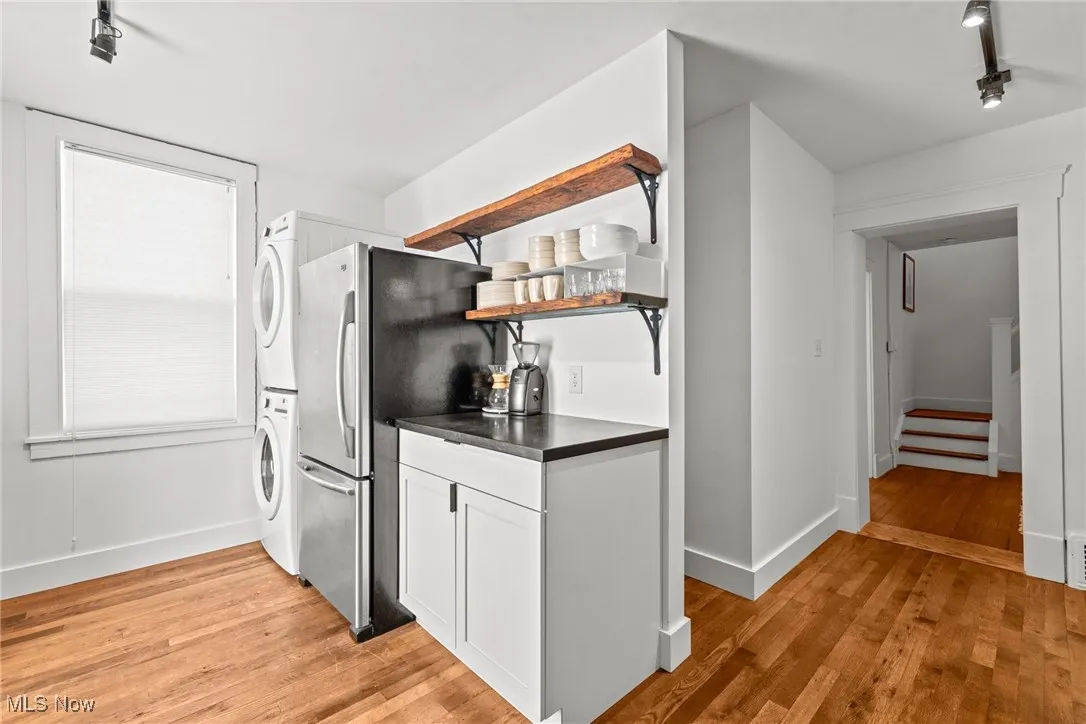 Kitchen with stacked washer and dryer, dark countertops, open shelves, and light wood-style floors