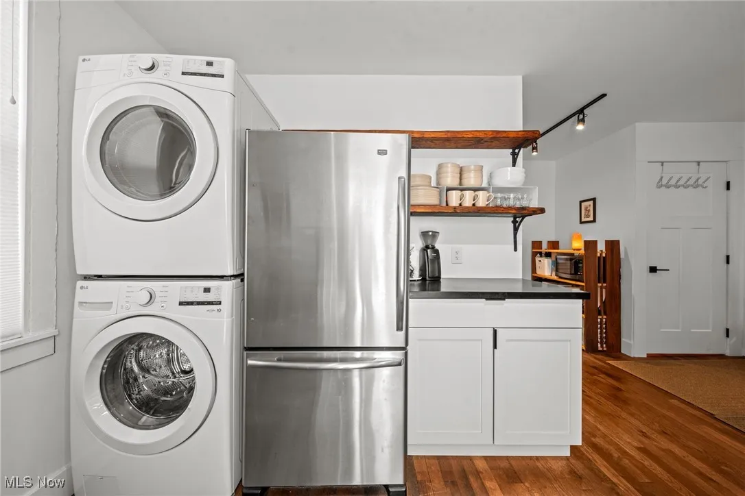 Laundry room with rail lighting, dark wood finished floors, and stacked washer / drying machine