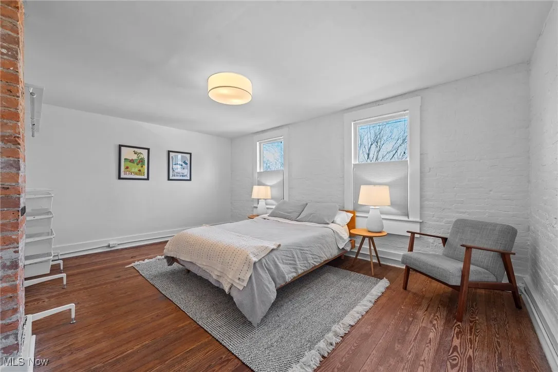 Bedroom with brick wall, baseboards, and wood finished floors