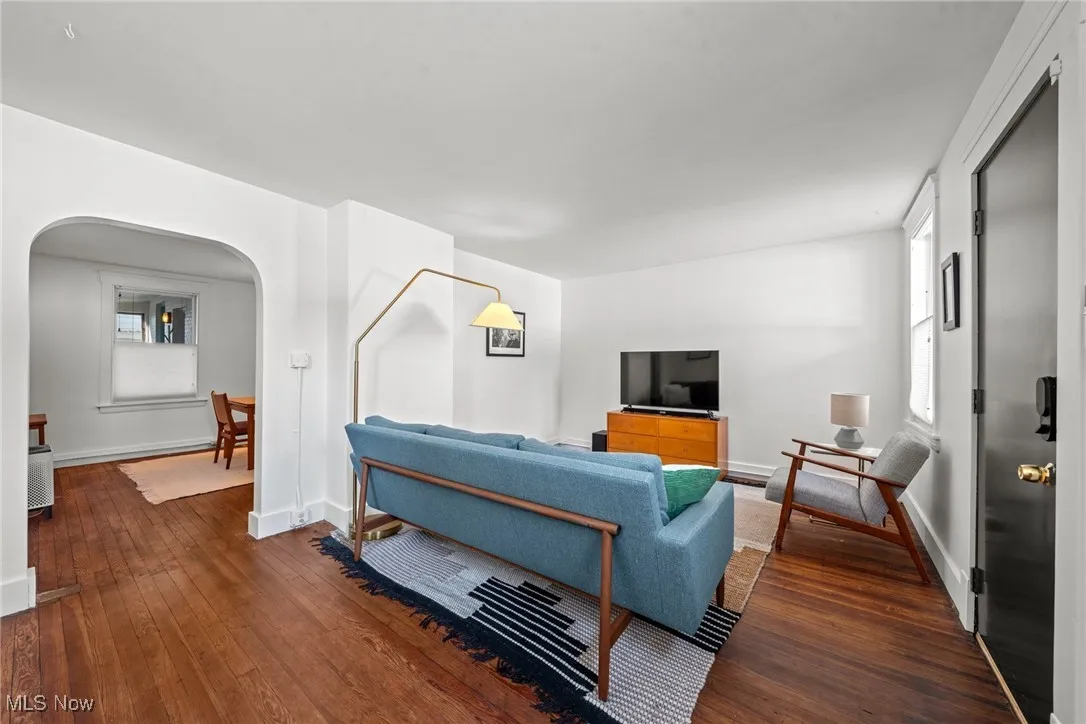 Living room with baseboards, arched walkways, and dark wood-style flooring