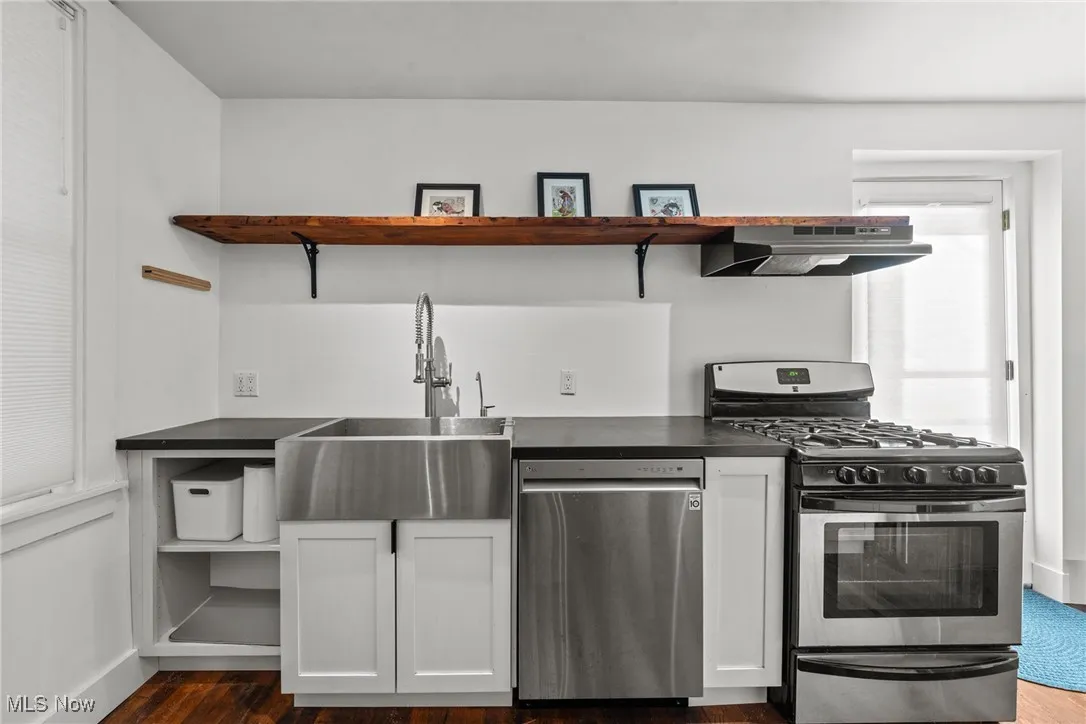 Kitchen featuring open shelves, under cabinet range hood, dark countertops, and stainless steel appliances