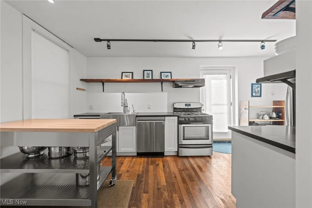 Kitchen featuring butcher block counters, dark wood-style flooring, a sink, appliances with stainless steel finishes, and open shelves