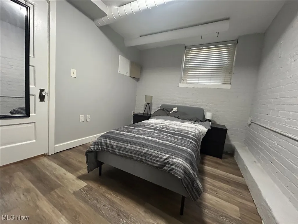 Bedroom with brick wall, baseboards, and wood finished floors