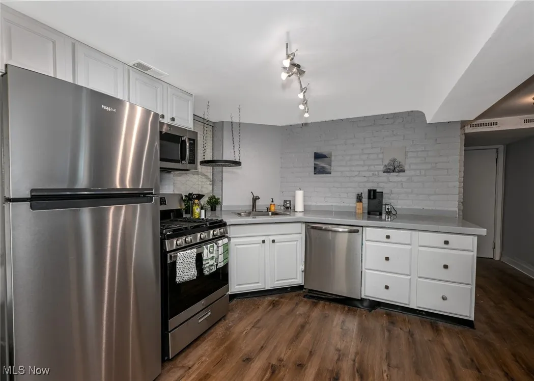 Kitchen featuring visible vents, a sink, dark wood-type flooring, white cabinets, and appliances with stainless steel finishes