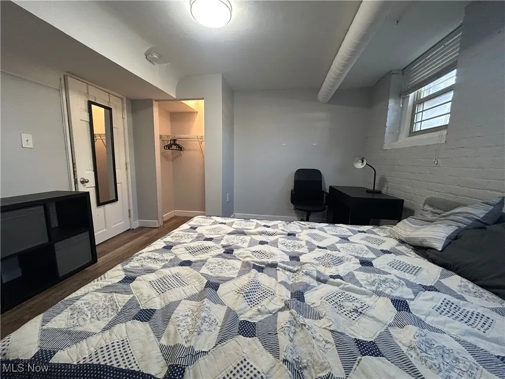 Bedroom with dark wood-style flooring, a closet, brick wall, baseboards, and a spacious closet