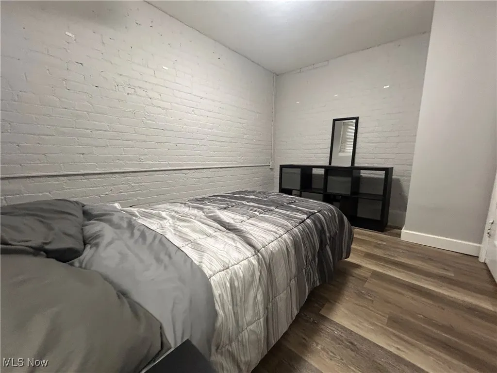 Bedroom featuring baseboards, wood finished floors, and brick wall