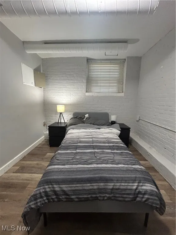 Bedroom with brick wall, baseboards, and wood finished floors