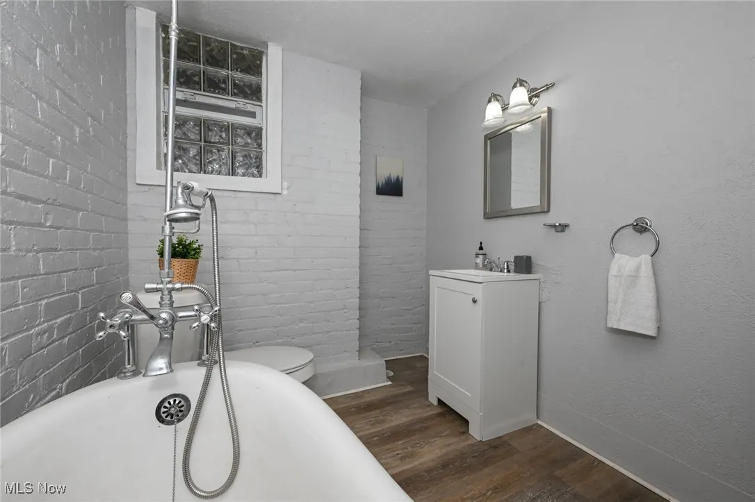Bathroom featuring a freestanding tub, brick wall, wood finished floors, and vanity