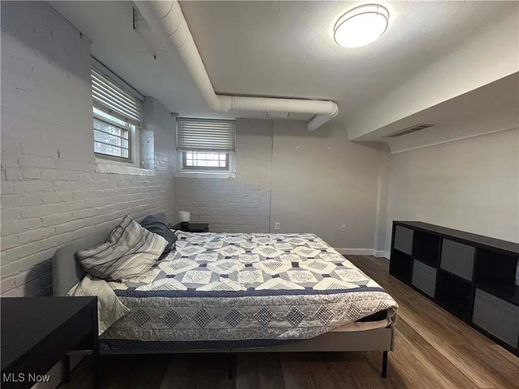 Bedroom with visible vents, brick wall, baseboards, and dark wood-style flooring