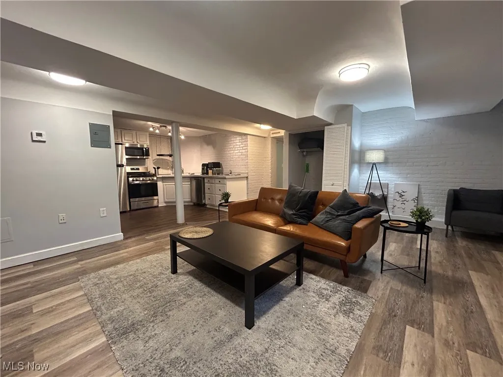 Living room featuring dark wood finished floors, brick wall, and baseboards
