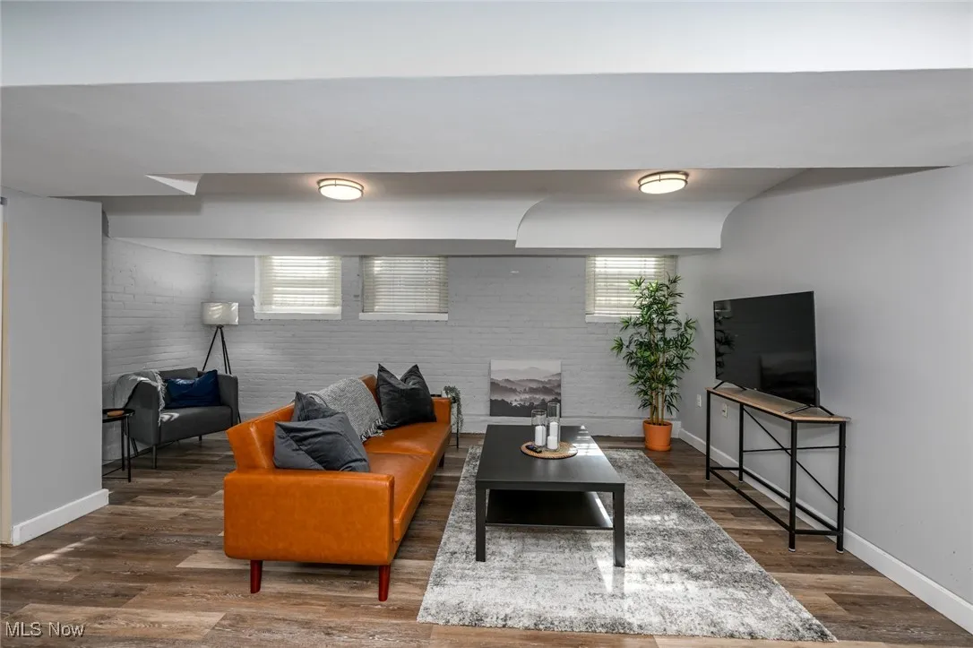 Living room featuring baseboards, wood finished floors, and brick wall