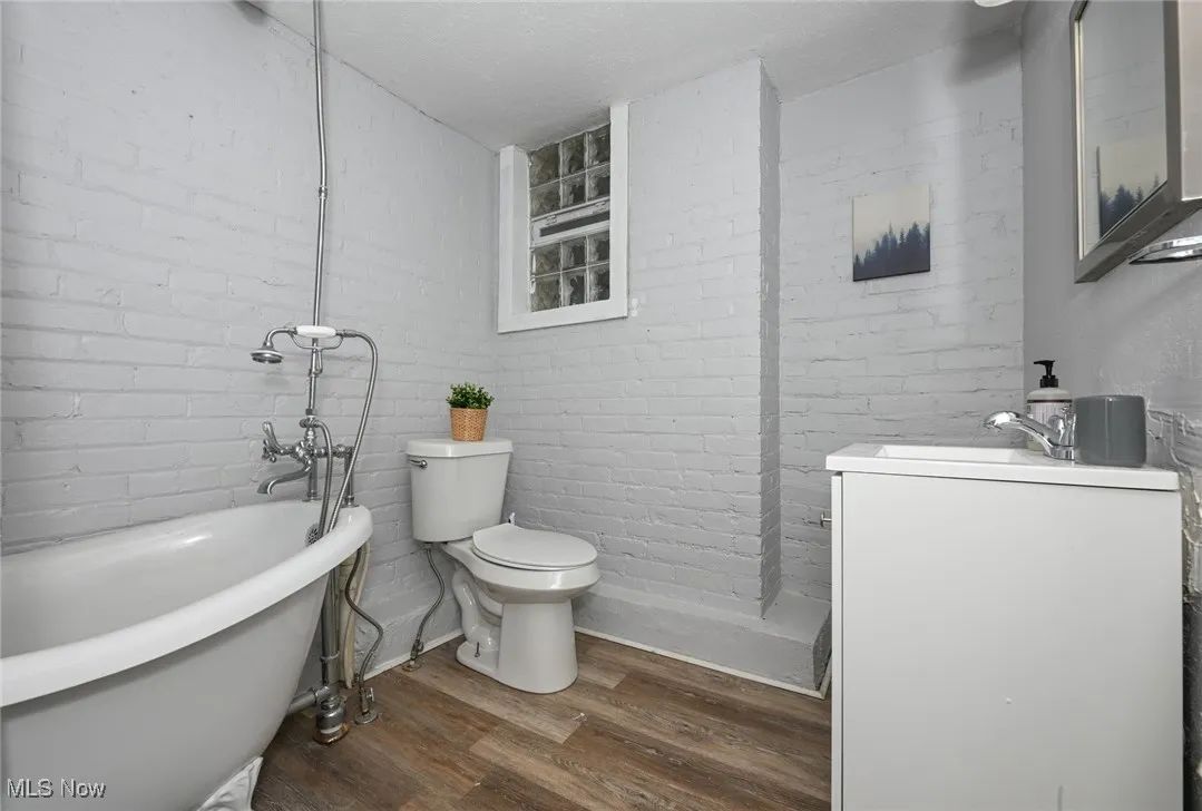 Full bath featuring a freestanding tub, toilet, wood finished floors, brick wall, and vanity