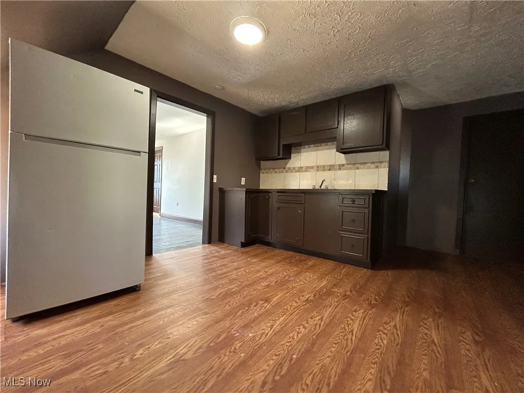Kitchen with backsplash, freestanding refrigerator, wood finished floors, a textured ceiling, and a sink