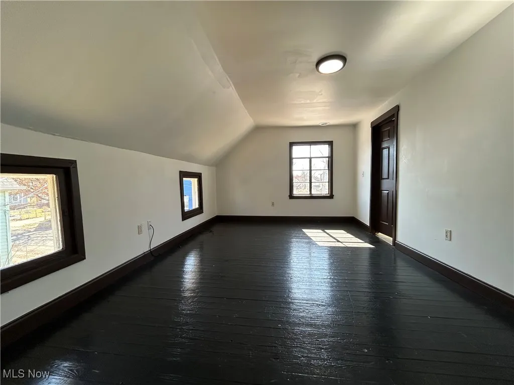 Bonus room with dark wood finished floors, vaulted ceiling, and baseboards